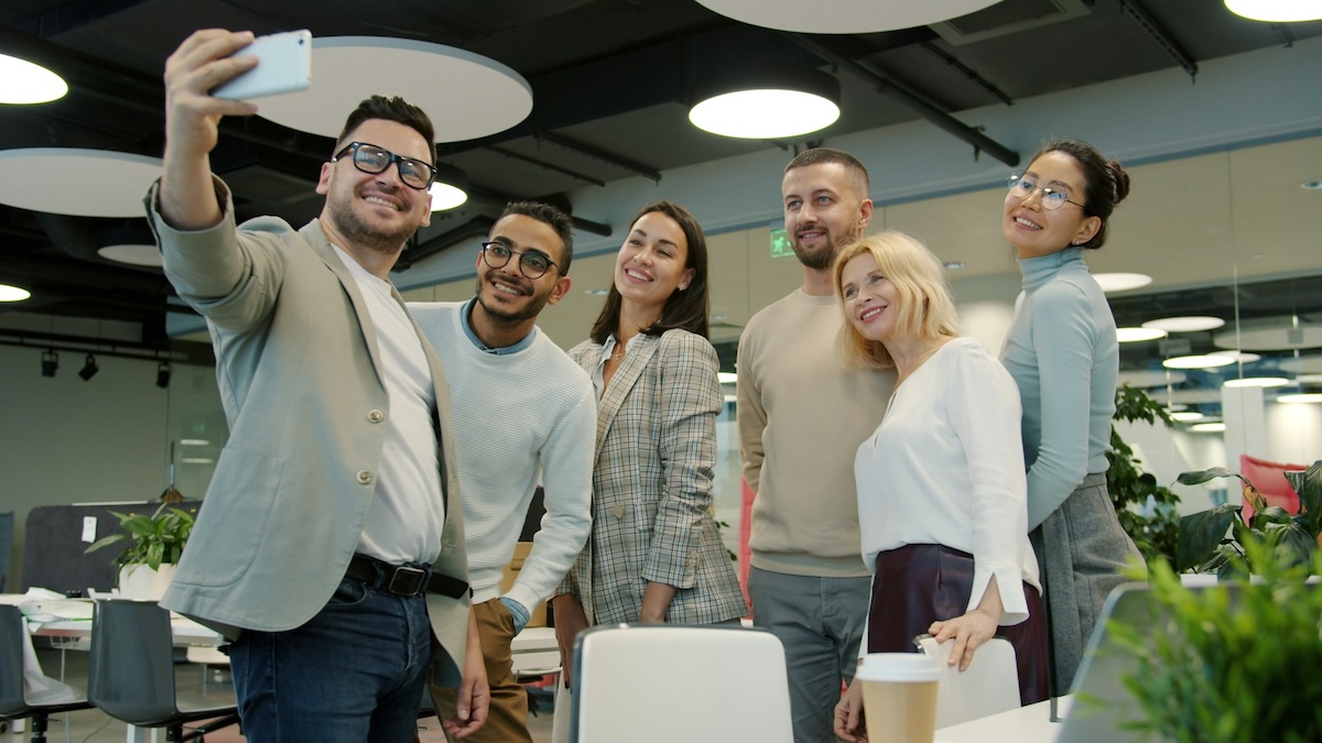 Photo of a team of six co-workers taking a selfie in an office.