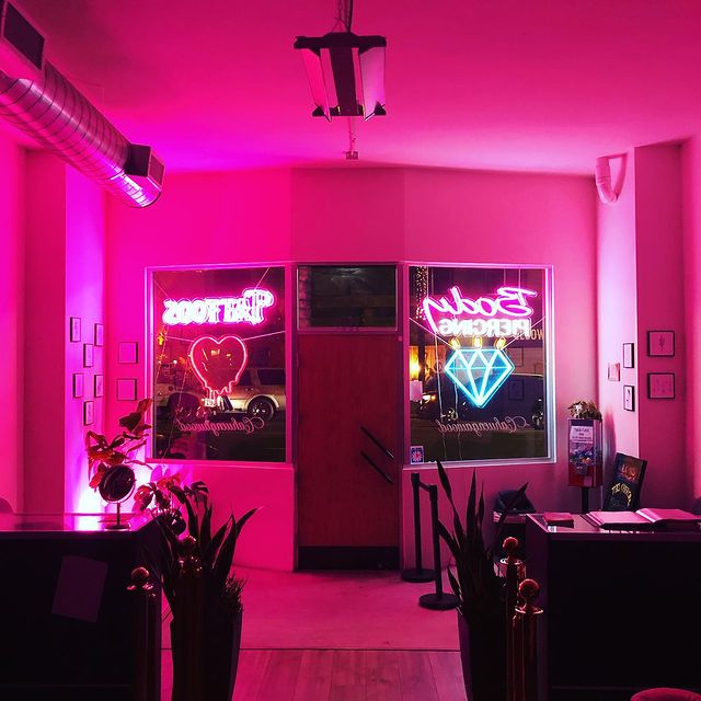 Office interior lit by pink neon lights, heart and diamond signs in the window.
