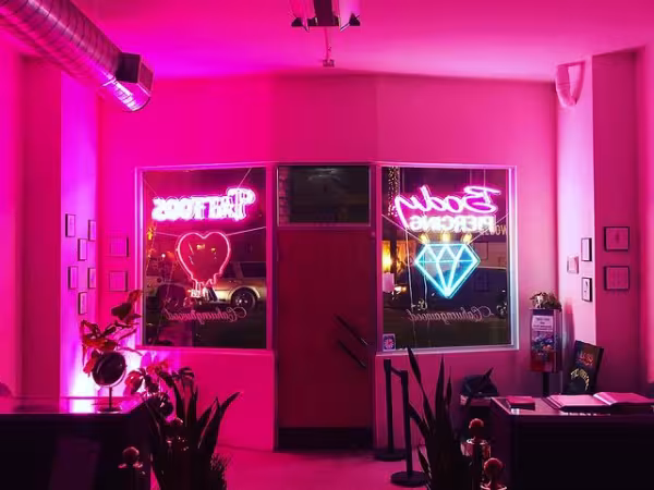 Office interior lit by pink neon lights, heart and diamond signs in the window.